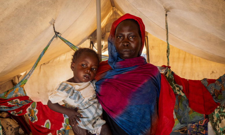 Woman in colorful shawl carrying a child on her back inside a tent.