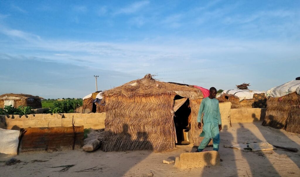 Traditional huts in a rural setting with a man walking by during sunset.