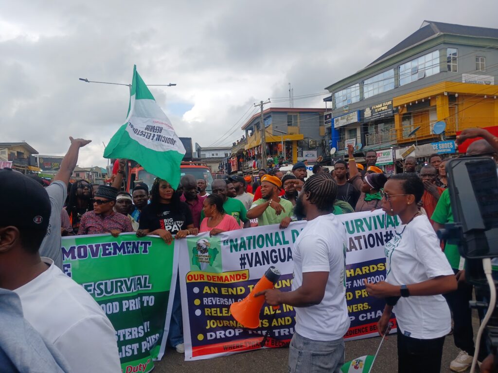 Group of people demonstrating, carrying banners and a flag, with buildings in the background.