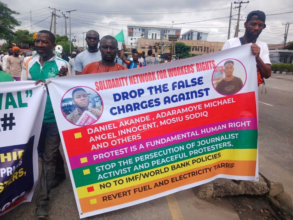 Group of individuals holding a protest banner calling for workers' rights and the dropping of false charges against activists.