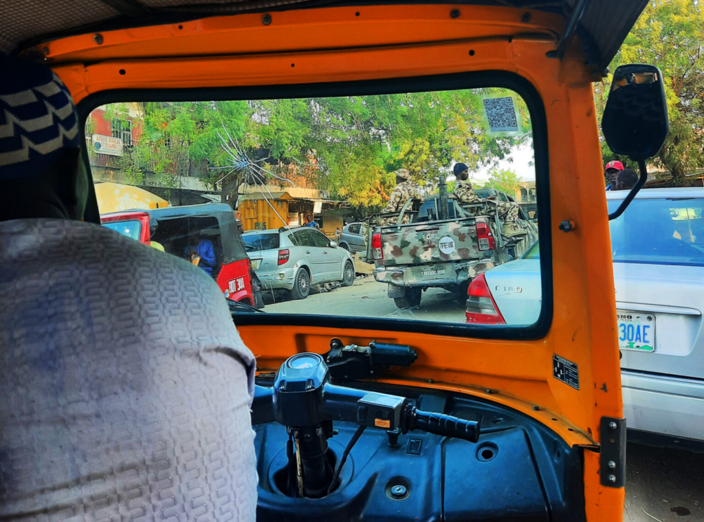 View from inside an auto rickshaw with a busy street scene, including a pickup truck with soldiers.