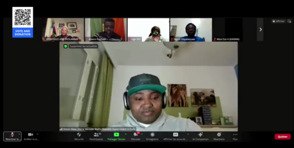 A video conference call with multiple participants, one prominently displayed, in a room with green walls and decor.