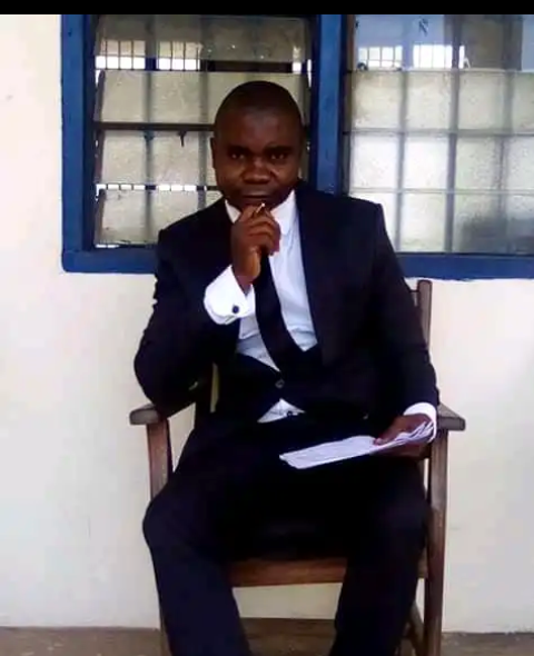 Man in a suit sitting on a chair, holding papers, with a contemplative expression.