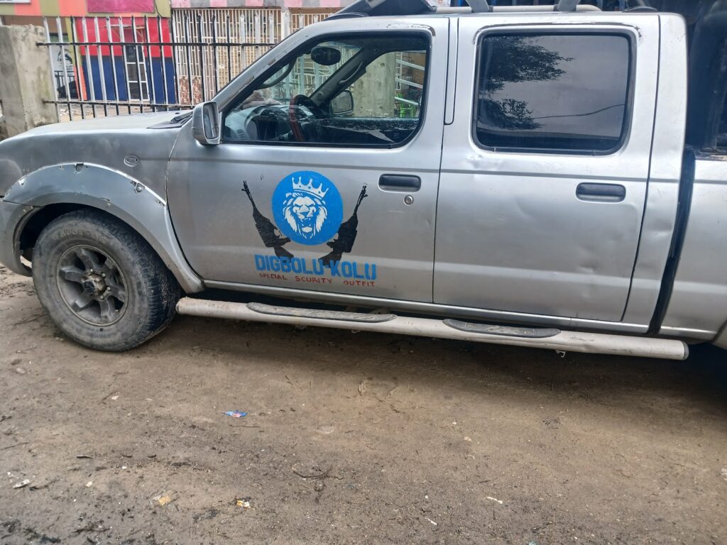 A gray pickup truck with a logo and text on its side parked on a dirt ground.