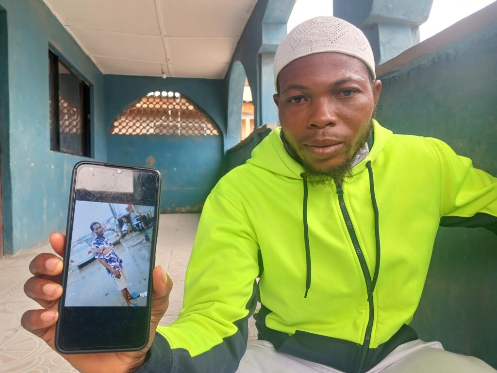 Man in neon jacket showing a phone with a cracked screen displaying a photo.