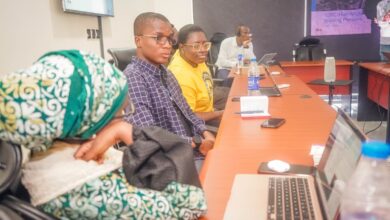 Three individuals focused on a presentation in a conference room with laptops and personal items on the table.