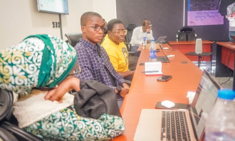 Three individuals focused on a presentation in a conference room with laptops and personal items on the table.