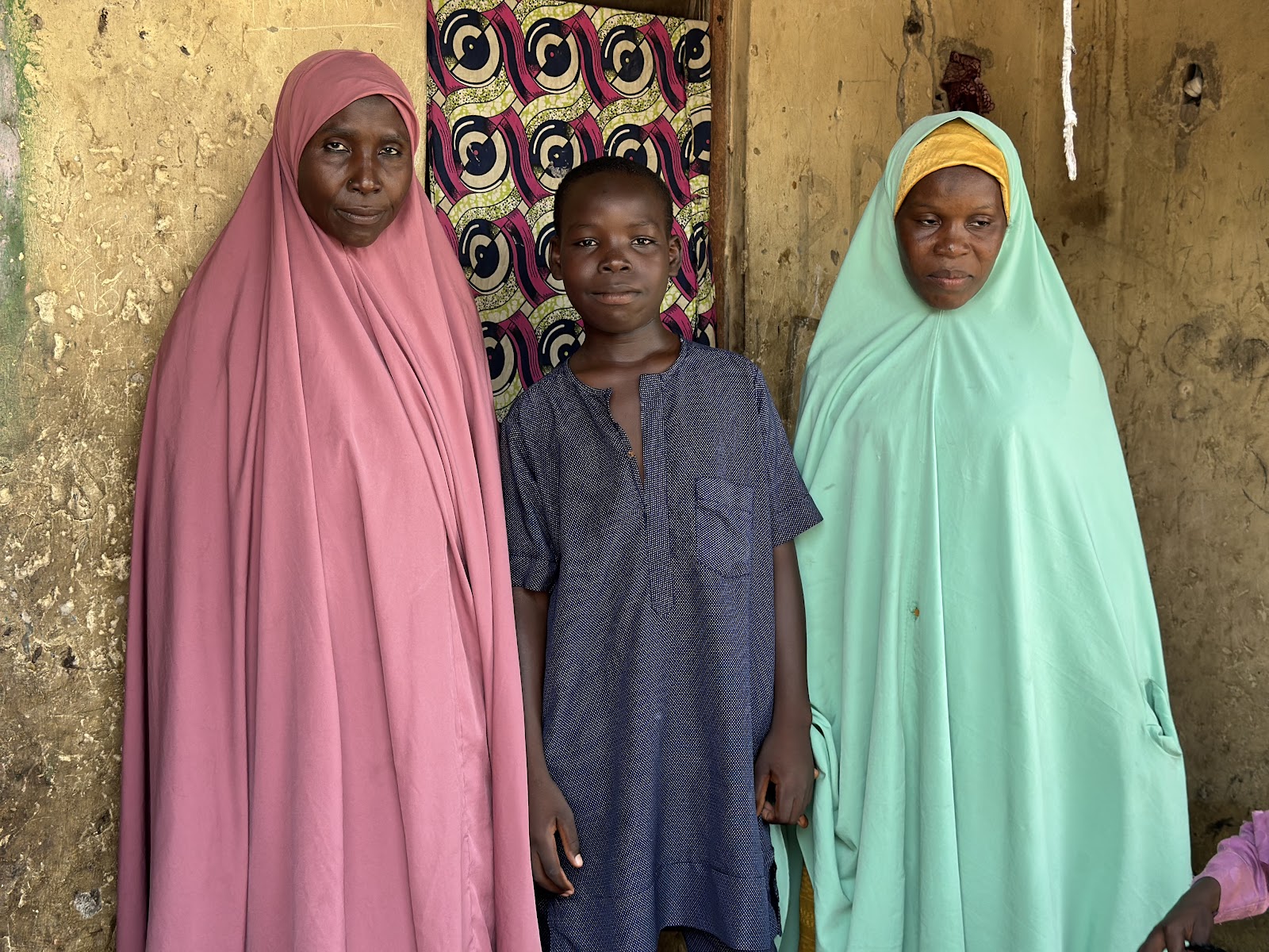 Two women in traditional clothing flanking a child by a textured wall.