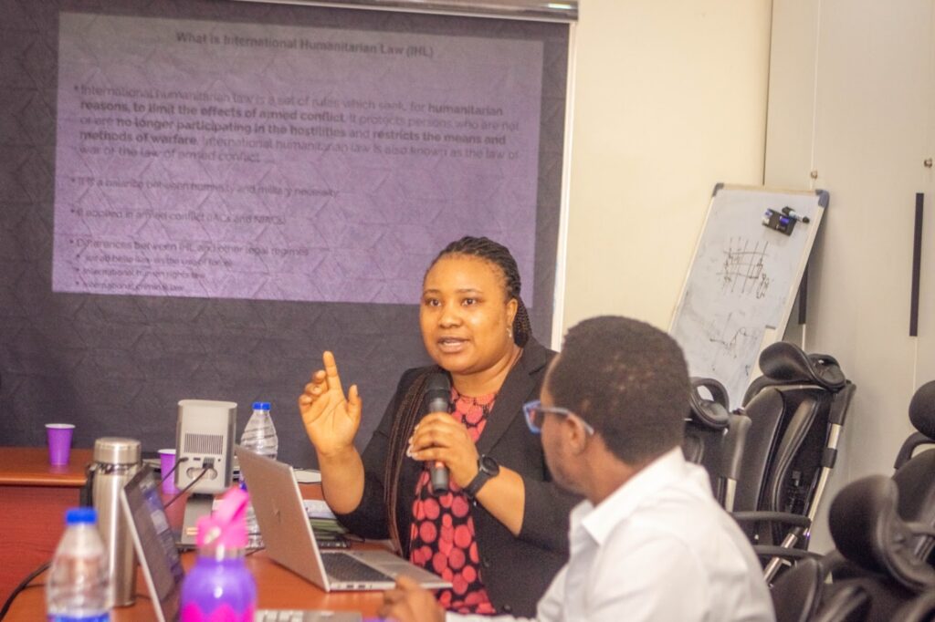 Woman presenting on International Humanitarian Law with attendees and a projector screen in a conference room.