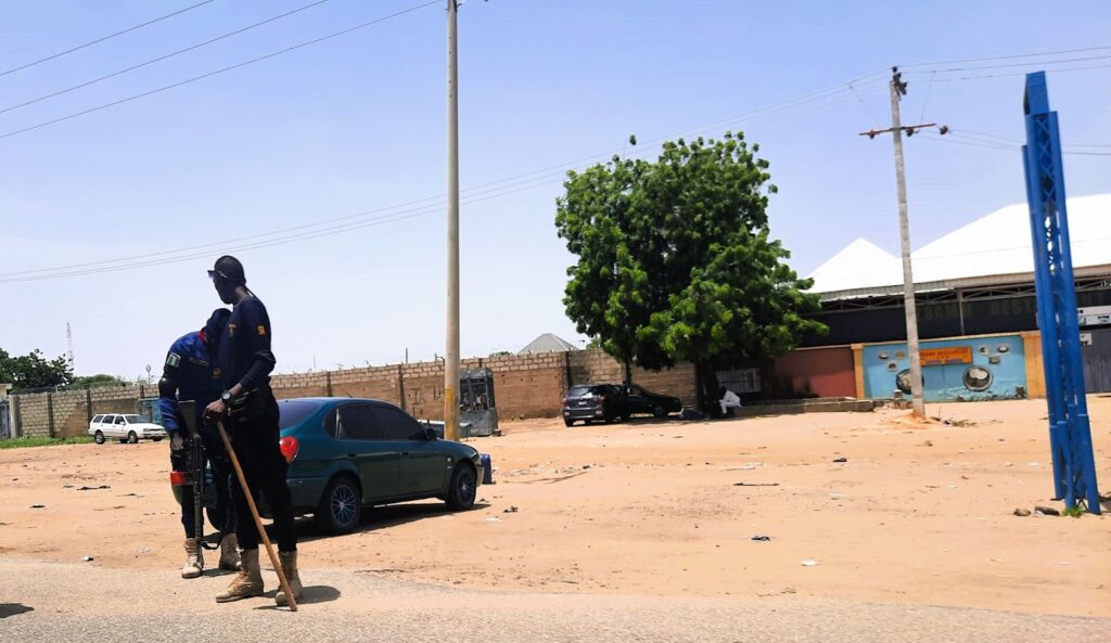 Security guard walking on a sandy street next to parked cars under a clear sky.