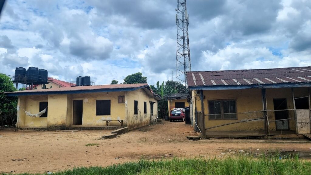 Rural landscape with two weathered buildings, a red car, and a cell tower under a cloudy sky.