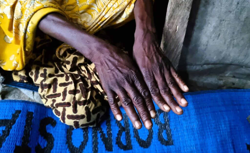 Close-up of a person's hands resting on blue fabric, with traditional patterns on their clothing.