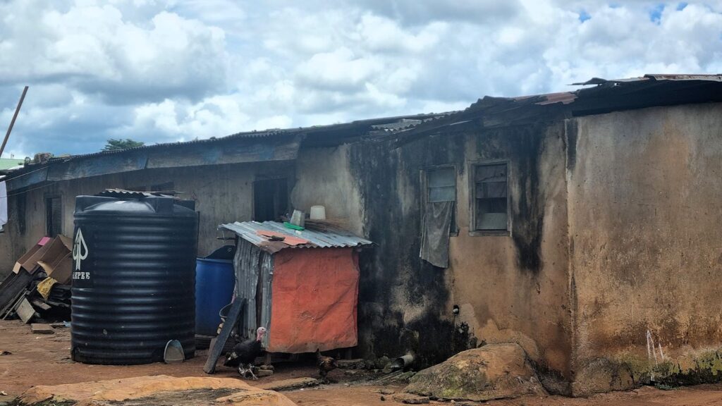 Dilapidated building with corrugated iron sheets and a water tank, under a cloudy sky.