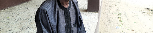 Person in a patterned jacket sitting on a bench with sand on the ground.