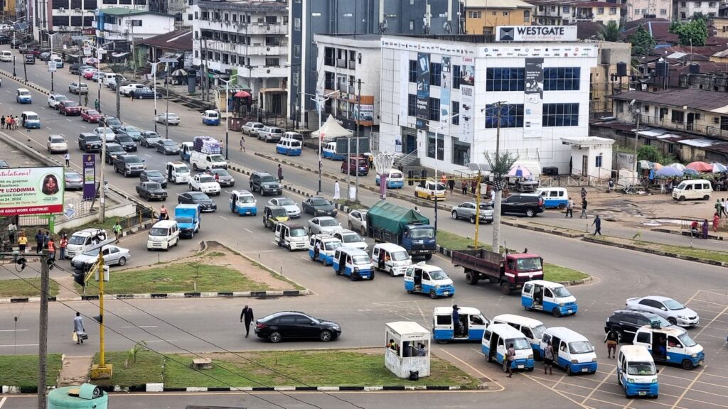 Busy urban street scene with mixed vehicular traffic and pedestrians near commercial buildings.