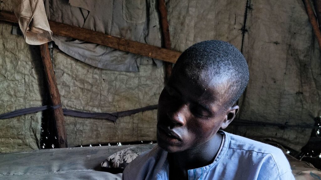 A person sitting pensively inside a dimly lit room with rustic interiors.