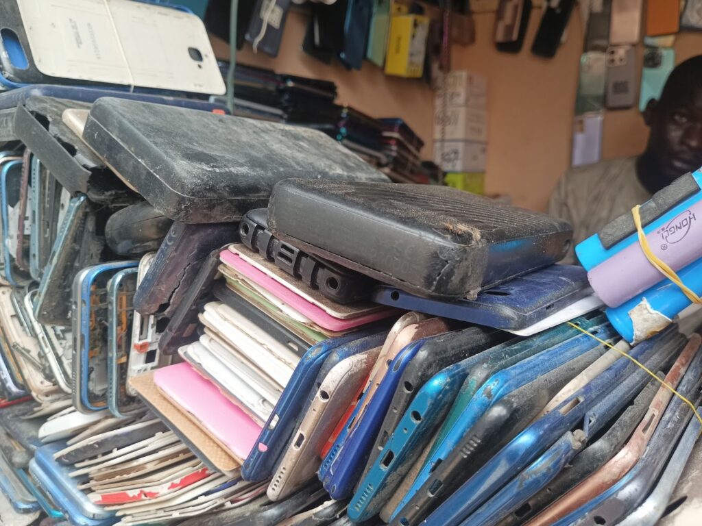 A pile of used mobile phones and batteries stacked haphazardly on a shelf.