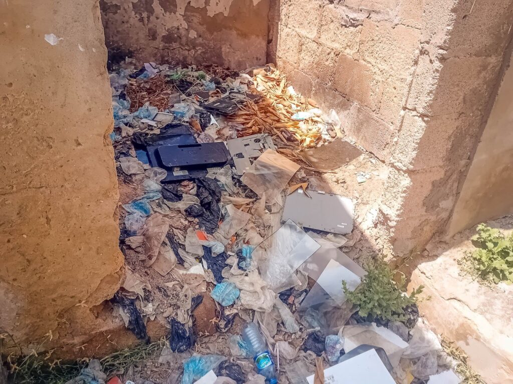 Corner of a dilapidated room filled with assorted garbage, debris, and fallen leaves.