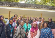 A diverse group of smiling women gathered for a group photo outdoors.