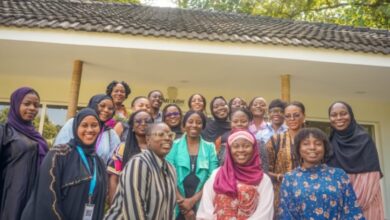 A diverse group of smiling women gathered for a group photo outdoors.