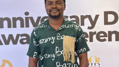 Man in traditional attire standing in front of a step-and-repeat banner.