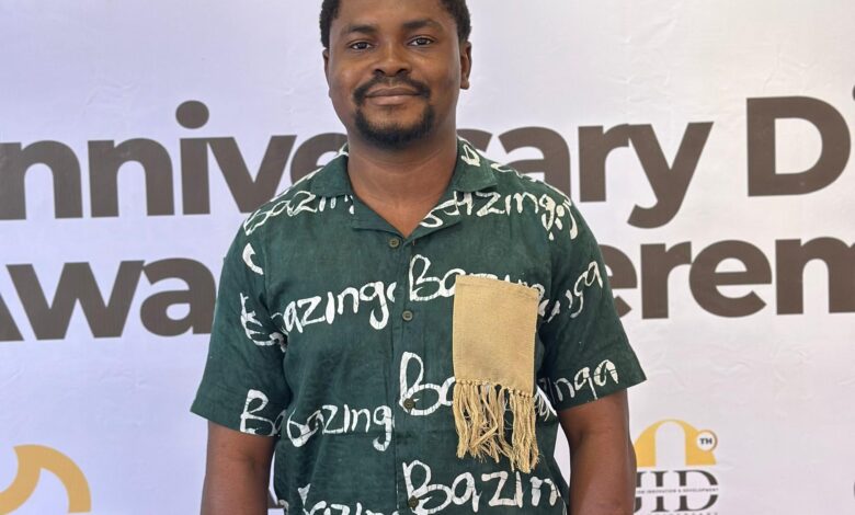 Man in traditional attire standing in front of a step-and-repeat banner.