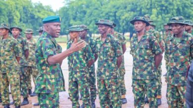 A group of soldiers in camouflage listening to an officer speaking outdoors.