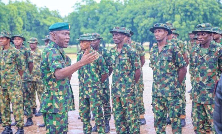 A group of soldiers in camouflage listening to an officer speaking outdoors.