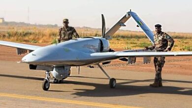 Two soldiers standing by a military drone on a runway.