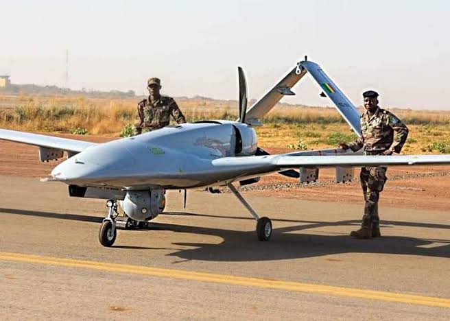 Two soldiers standing by a military drone on a runway.