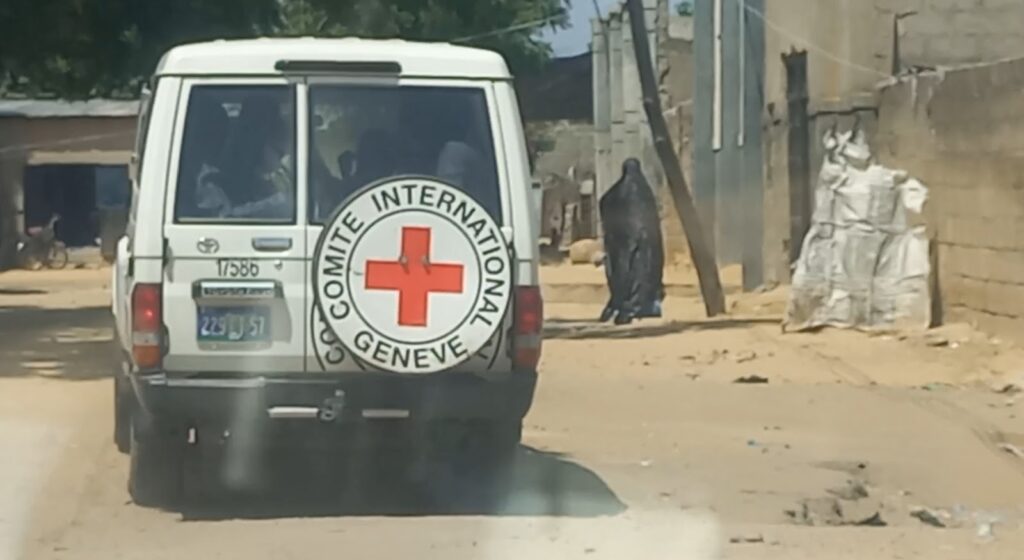 ICRC vehicle on a dusty street, signaling humanitarian presence in a developing area.