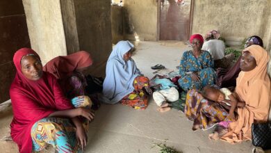 Group of women sitting on the floor in traditional attire with a child sleeping on one of the women's lap.