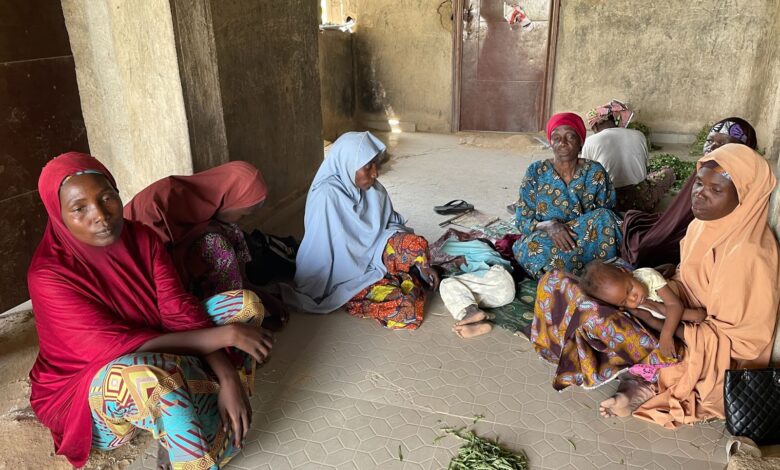 Group of women sitting on the floor in traditional attire with a child sleeping on one of the women's lap.