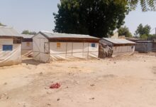 Aid tents with EU and NRC logos in a dry, sandy area with sparse vegetation.