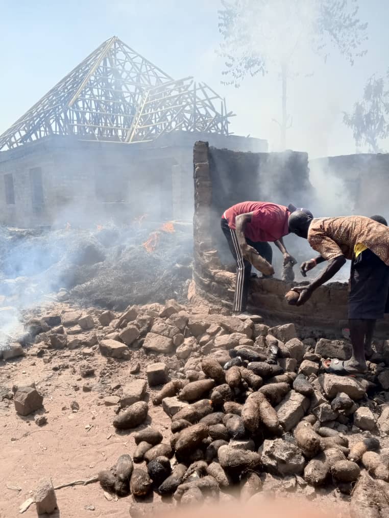 People near a collapsed building with smoldering debris under a hazy sky.