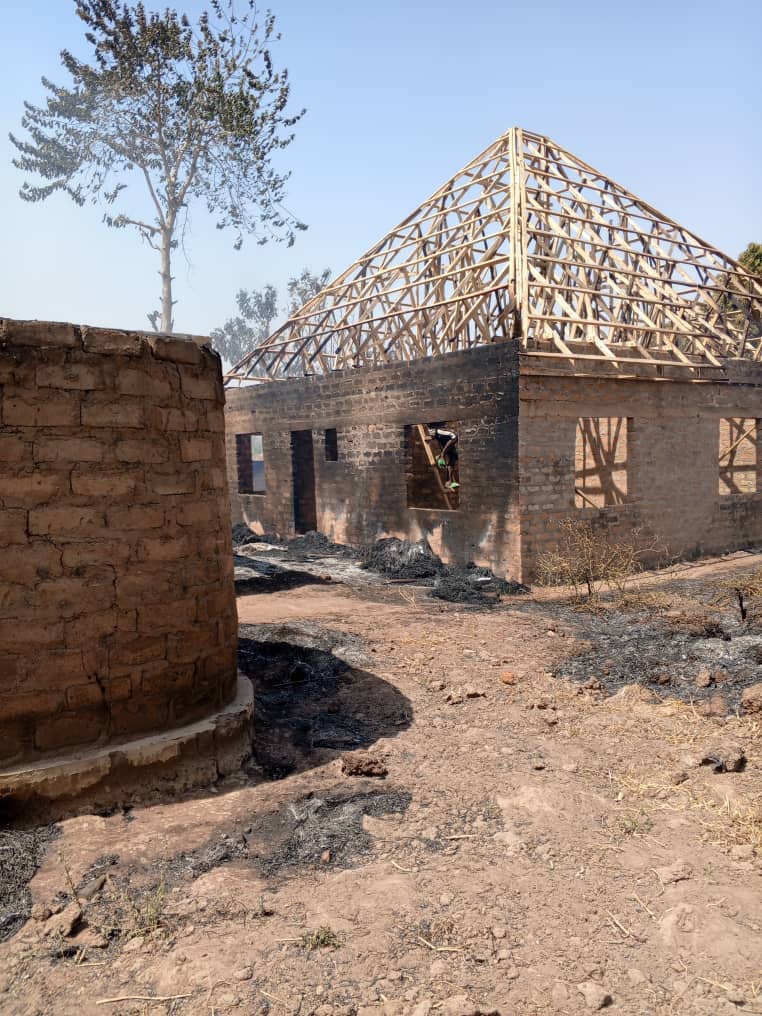 Unfinished brick building with exposed wooden roof framework and scorched ground nearby.