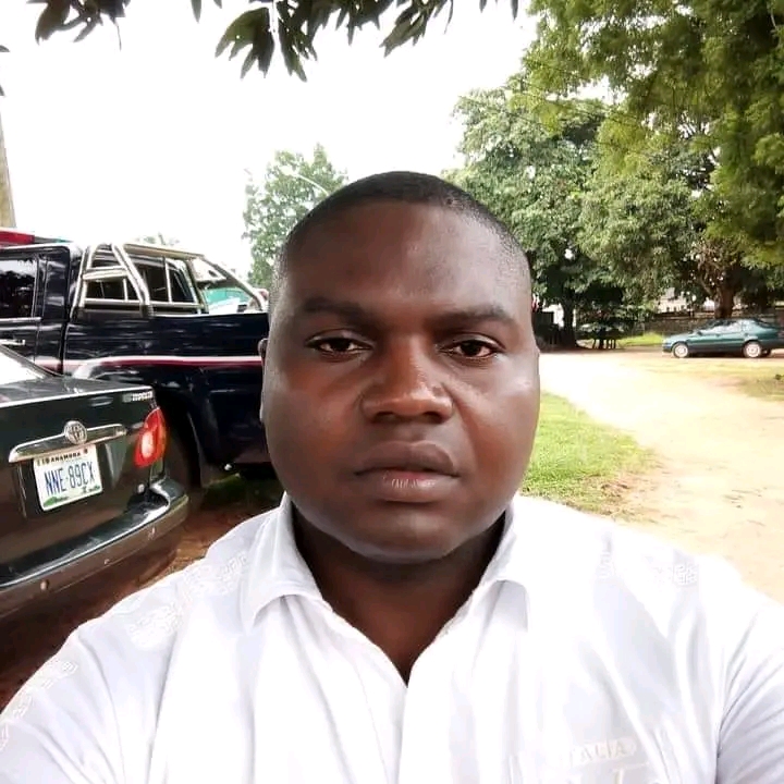 A man in a white shirt taking a selfie with a tree and parked cars in the background.