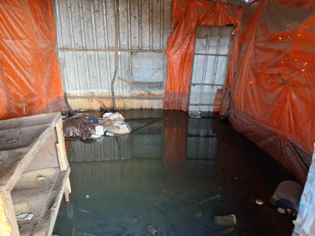 Flooded indoor space with debris, waterlogged items, and orange tarps hanging from the walls.