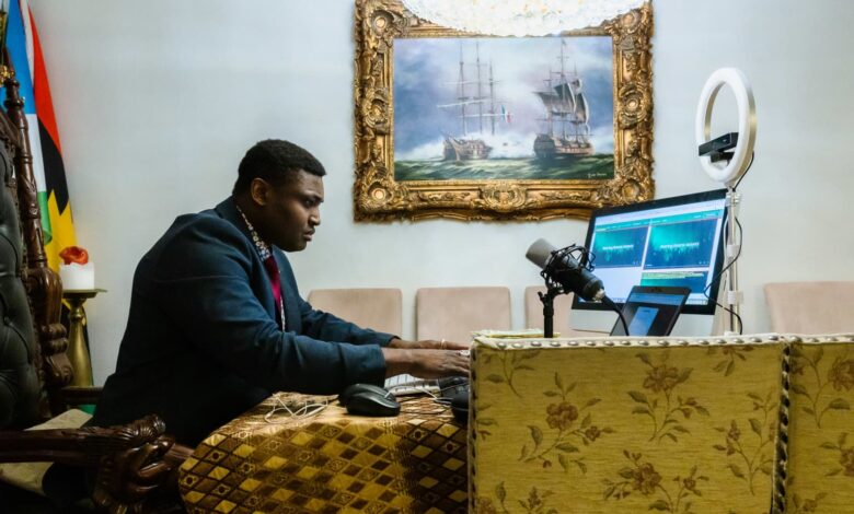 Man in a suit podcasting with a mic and laptop in a room with a classic painting and a ring light.