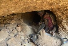 Person in a tunnel shoveling earth into a pan, surrounded by dirt and rocks.