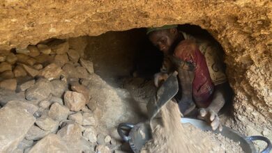 Person in a tunnel shoveling earth into a pan, surrounded by dirt and rocks.