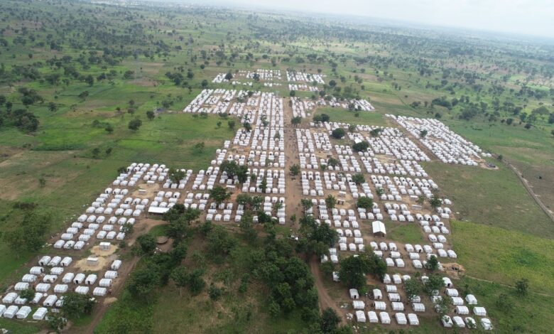 Aerial view of a large refugee camp with rows of white tents scattered across a green landscape.