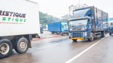 Trucks driving on a wet road with "TOURISTIQUE LOGISTIQUE" printed on the side of one vehicle.