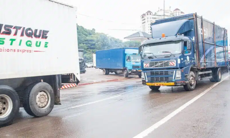 Trucks driving on a wet road with "TOURISTIQUE LOGISTIQUE" printed on the side of one vehicle.