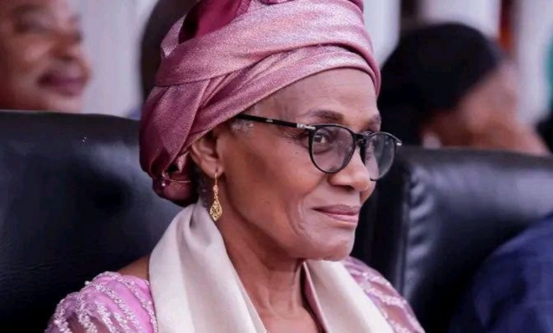 Elderly woman smiling, wearing glasses, pink headscarf, and earrings.