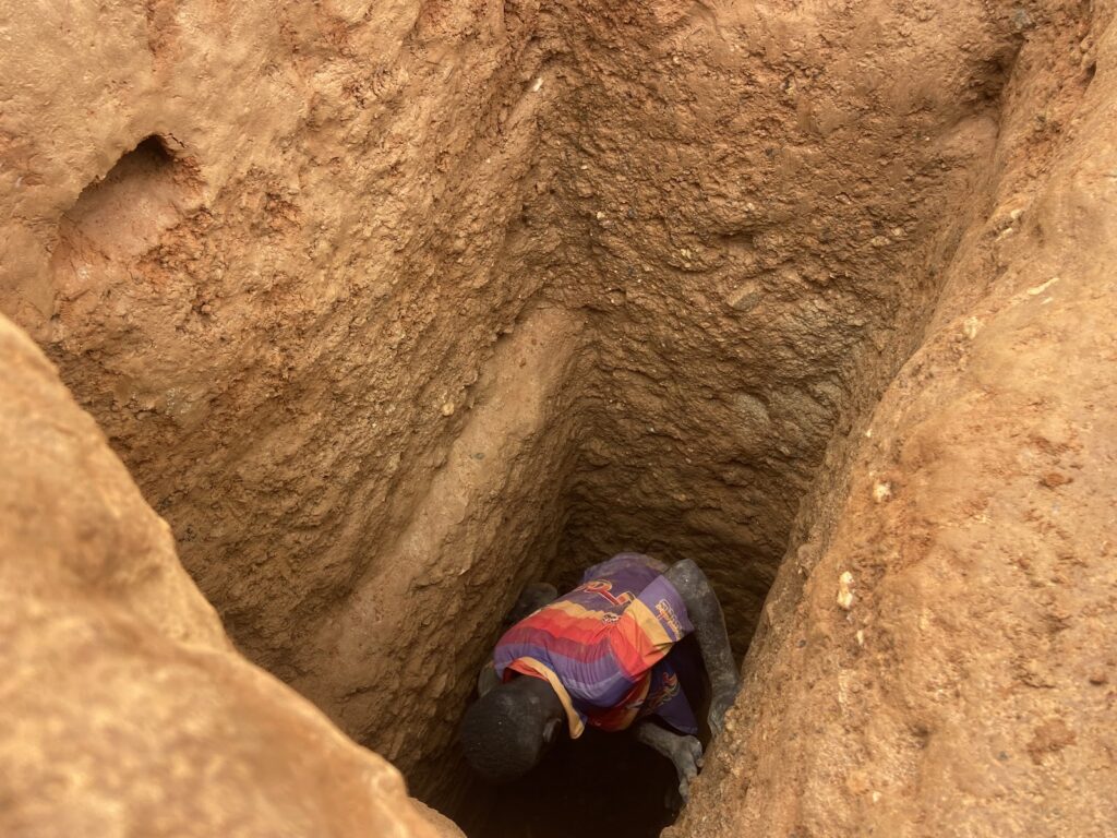 A person climbing down a narrow, earthen pit or tunnel.