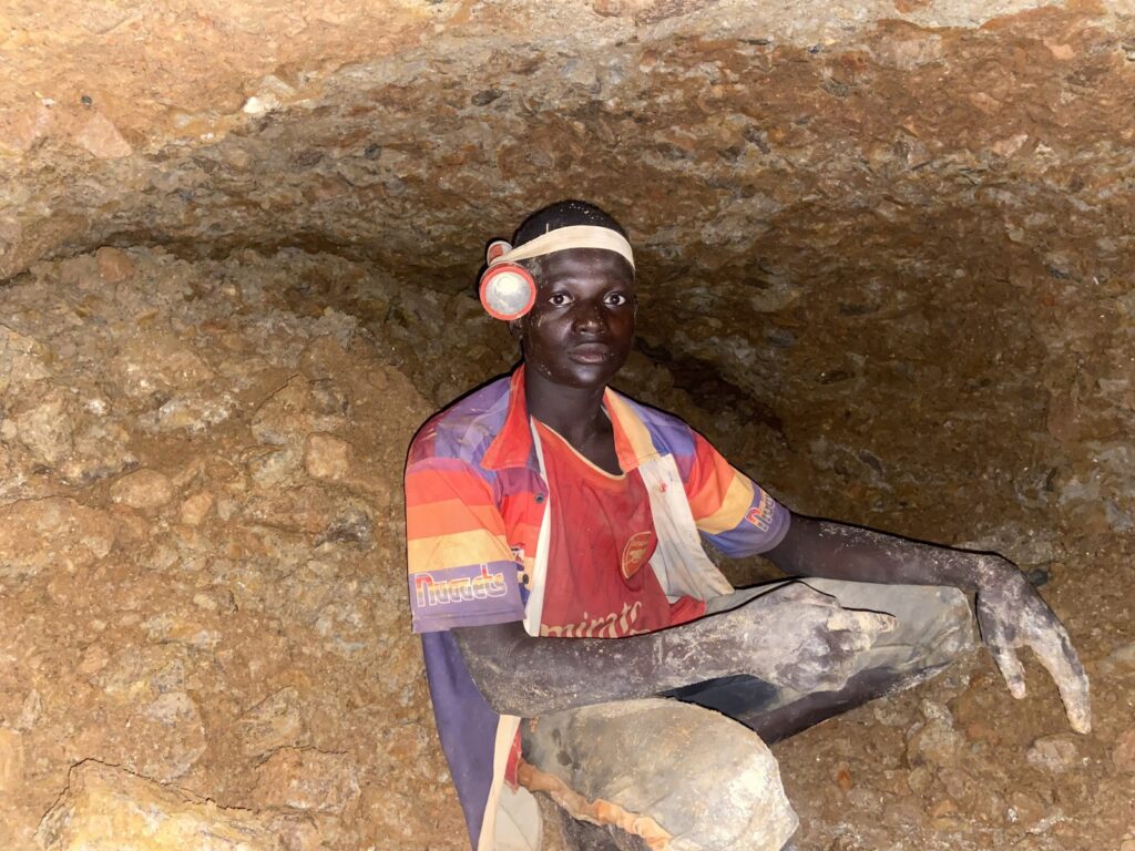 Miner with headlamp sitting in a rocky tunnel.