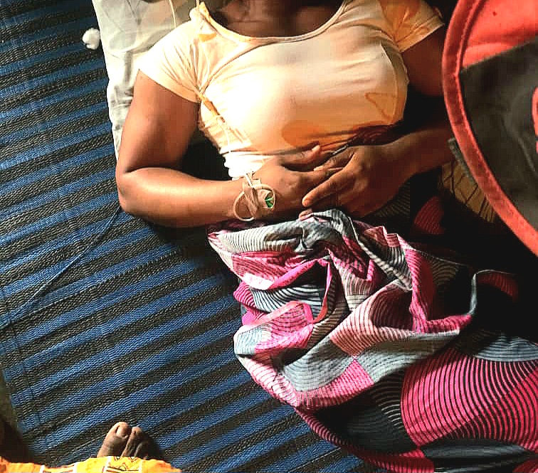 Person lying on a striped mat with an IV in their hand, surrounded by colorful textiles.