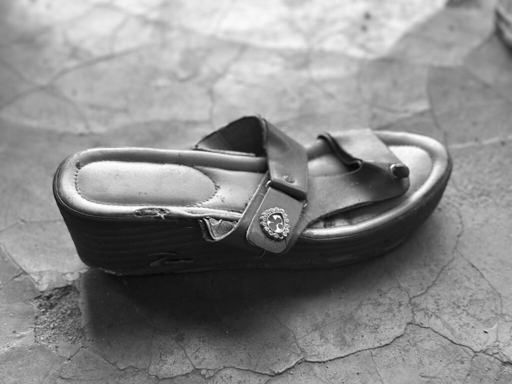 A single worn-out sandal on a cracked floor in black and white.