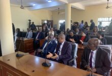 A courtroom scene with attendees seated, some listening intently with focused expressions.